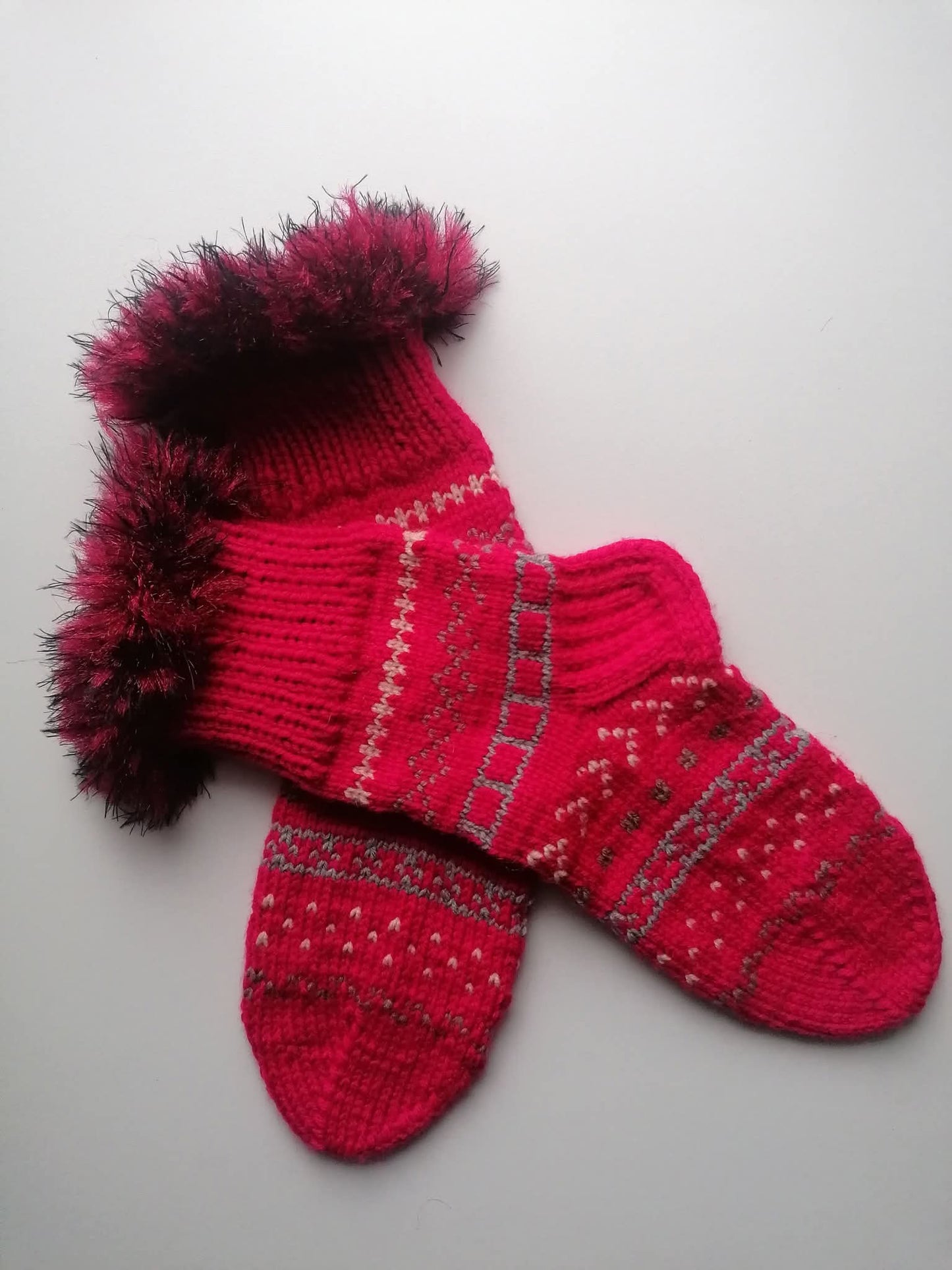 Pair of red fluffy knitted socks with a pattern on a light gray background