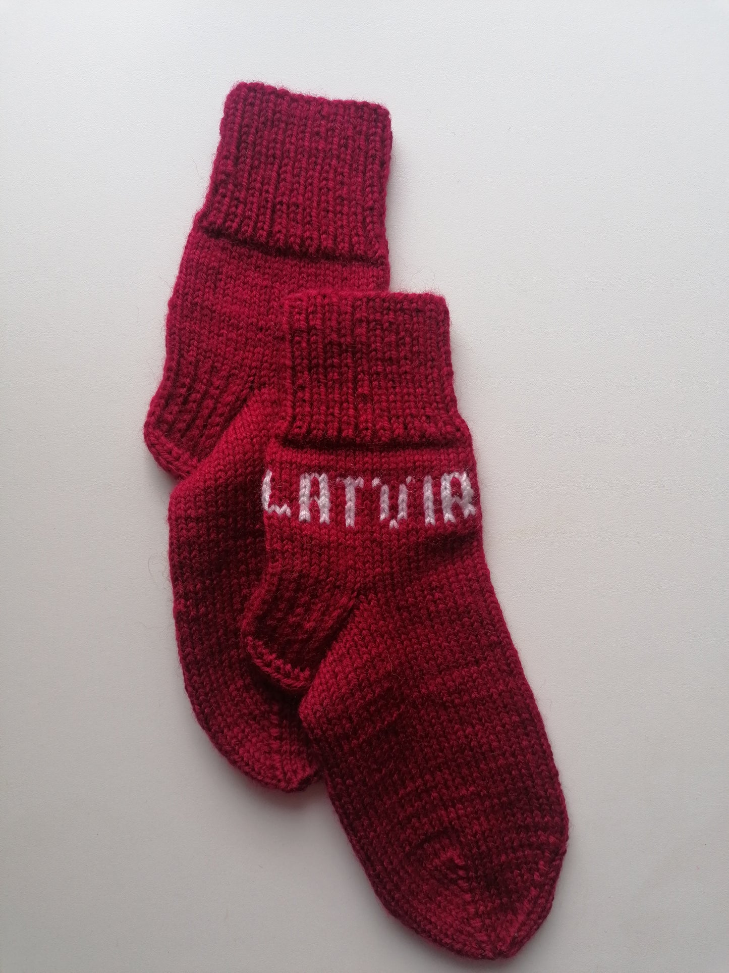 Red knitted socks with 'Latvia' text on a light gray background