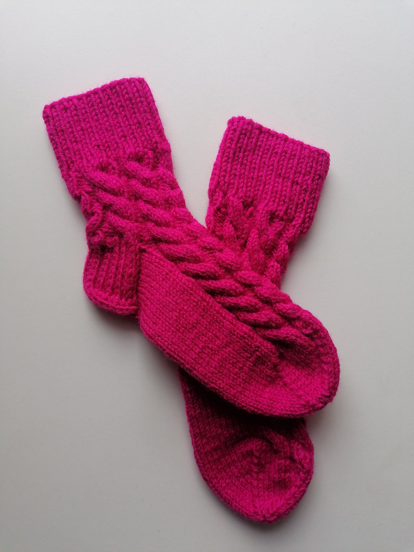 Pair of pink knitted socks wiht braids on a light gray background