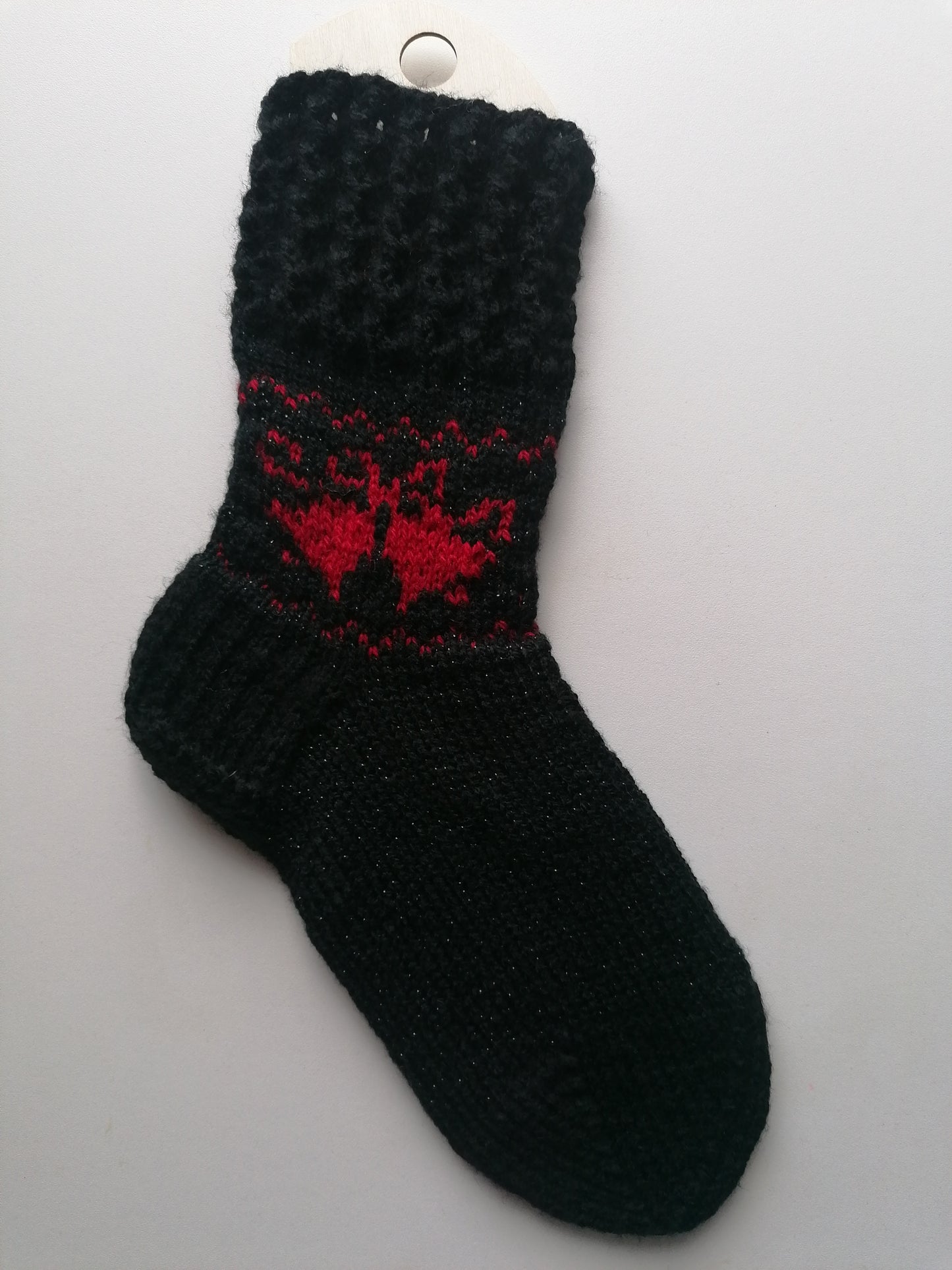 Black knit sock with red pattern Christmas bells on a white background