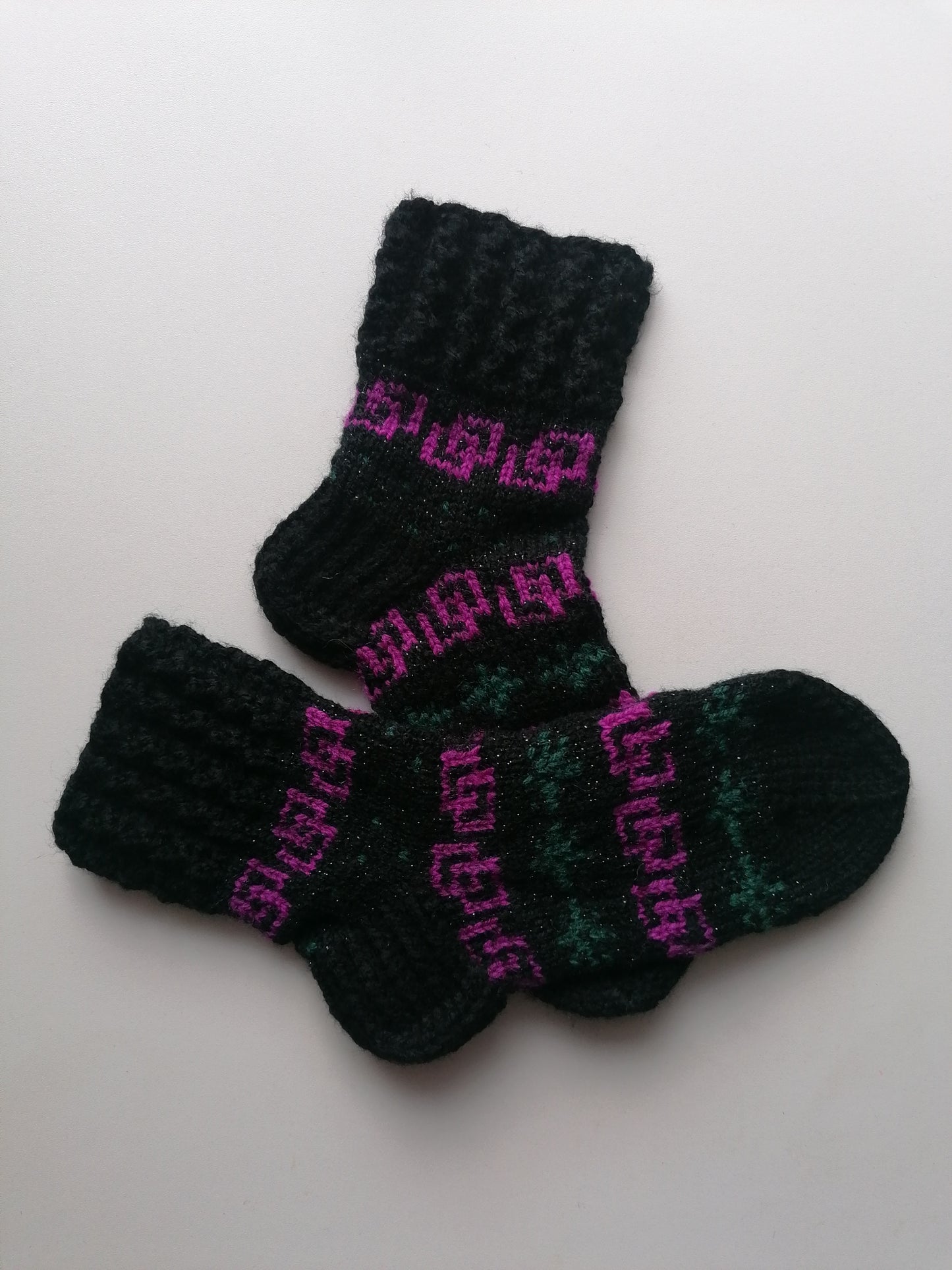 Pair of black and green knitted socks with pink text on a white background