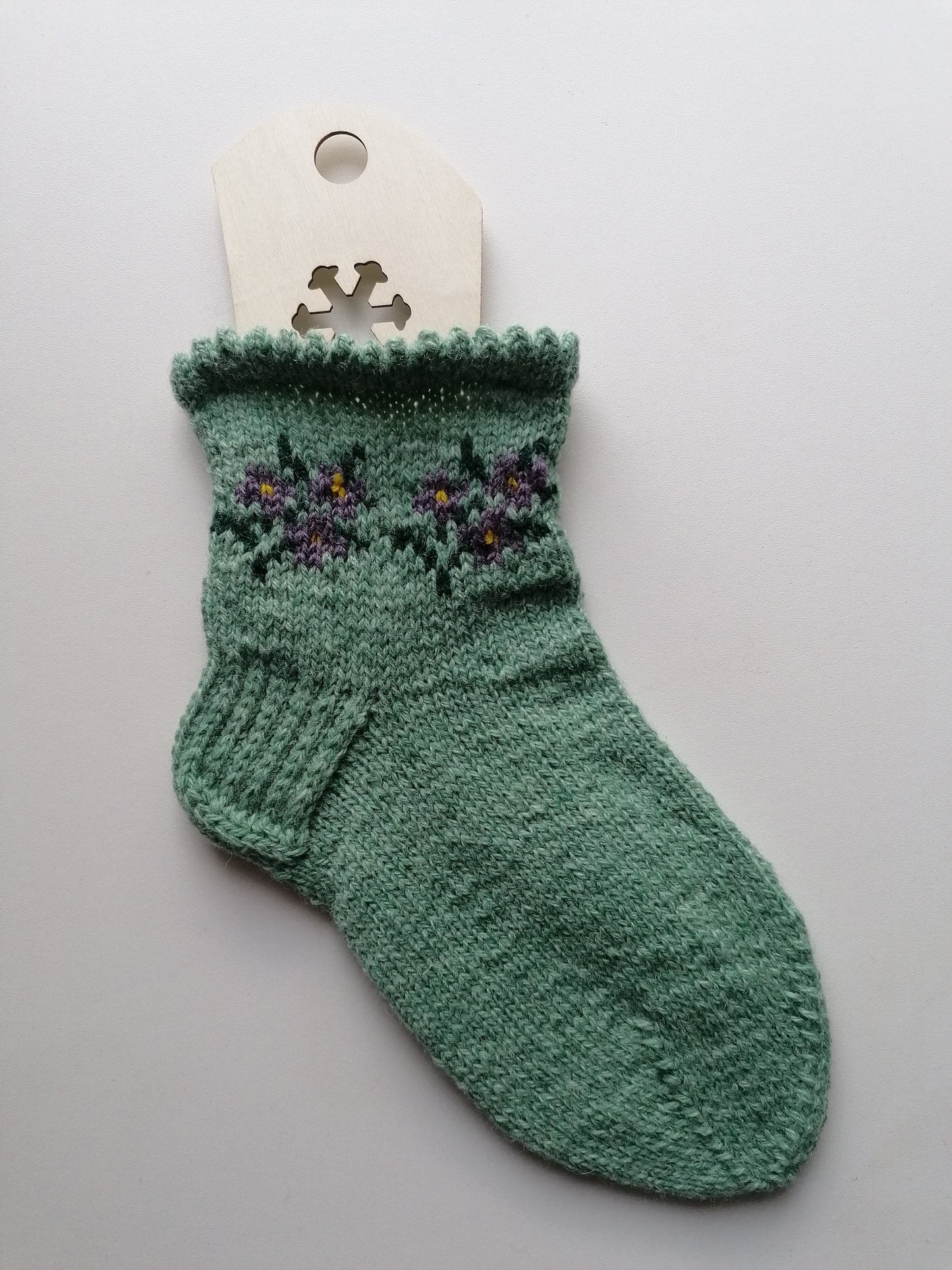 Green knitted sock with floral patterns on a white background