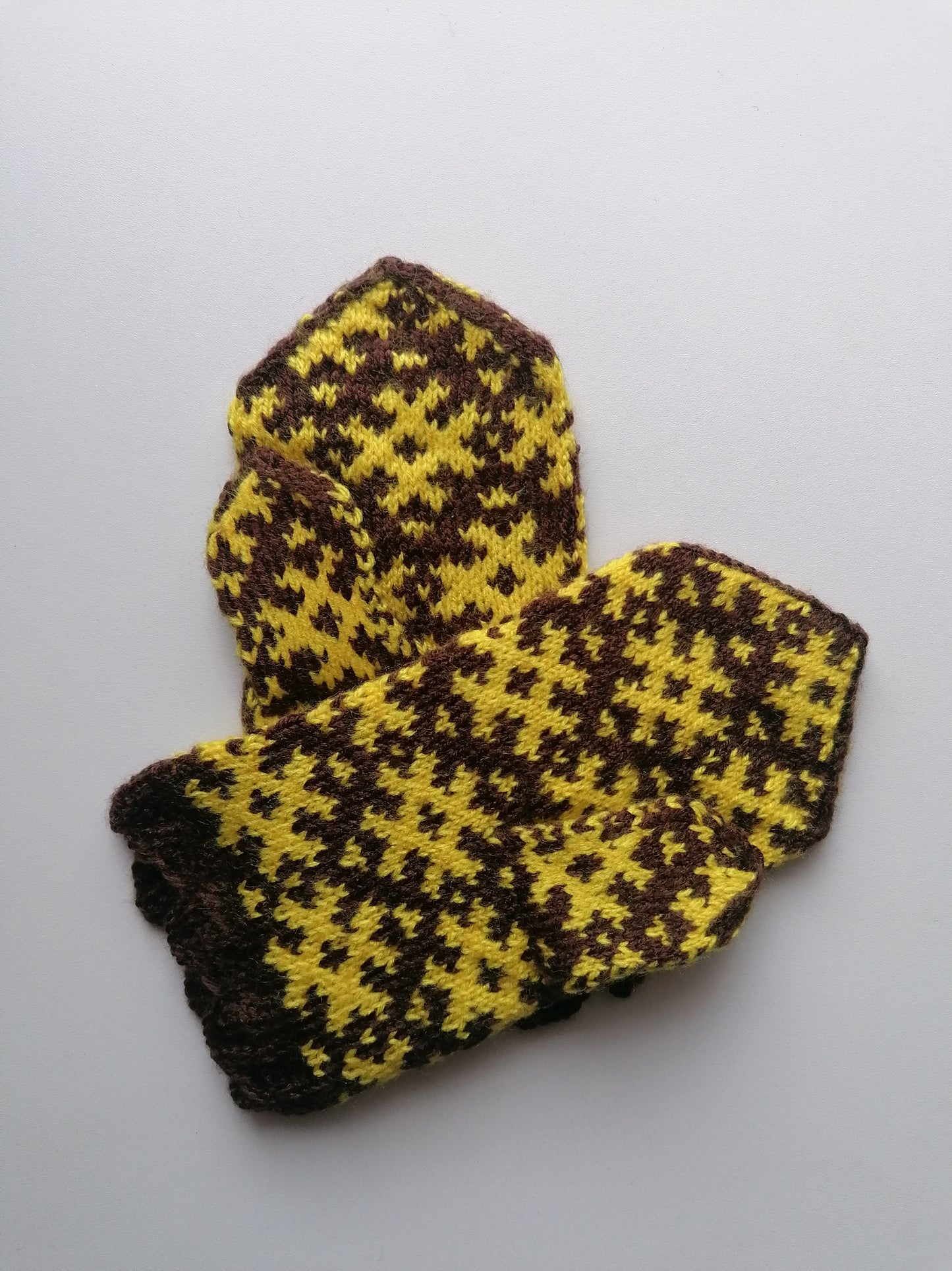 Pair of brown and yellow houndstooth patterned mittens on a light gray background