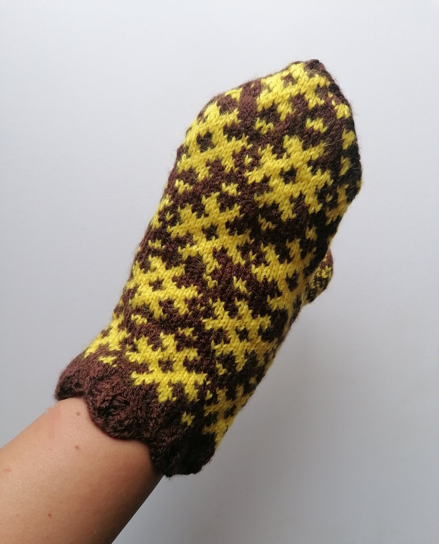 Knitted mitten with brown and yellow pattern on a white background