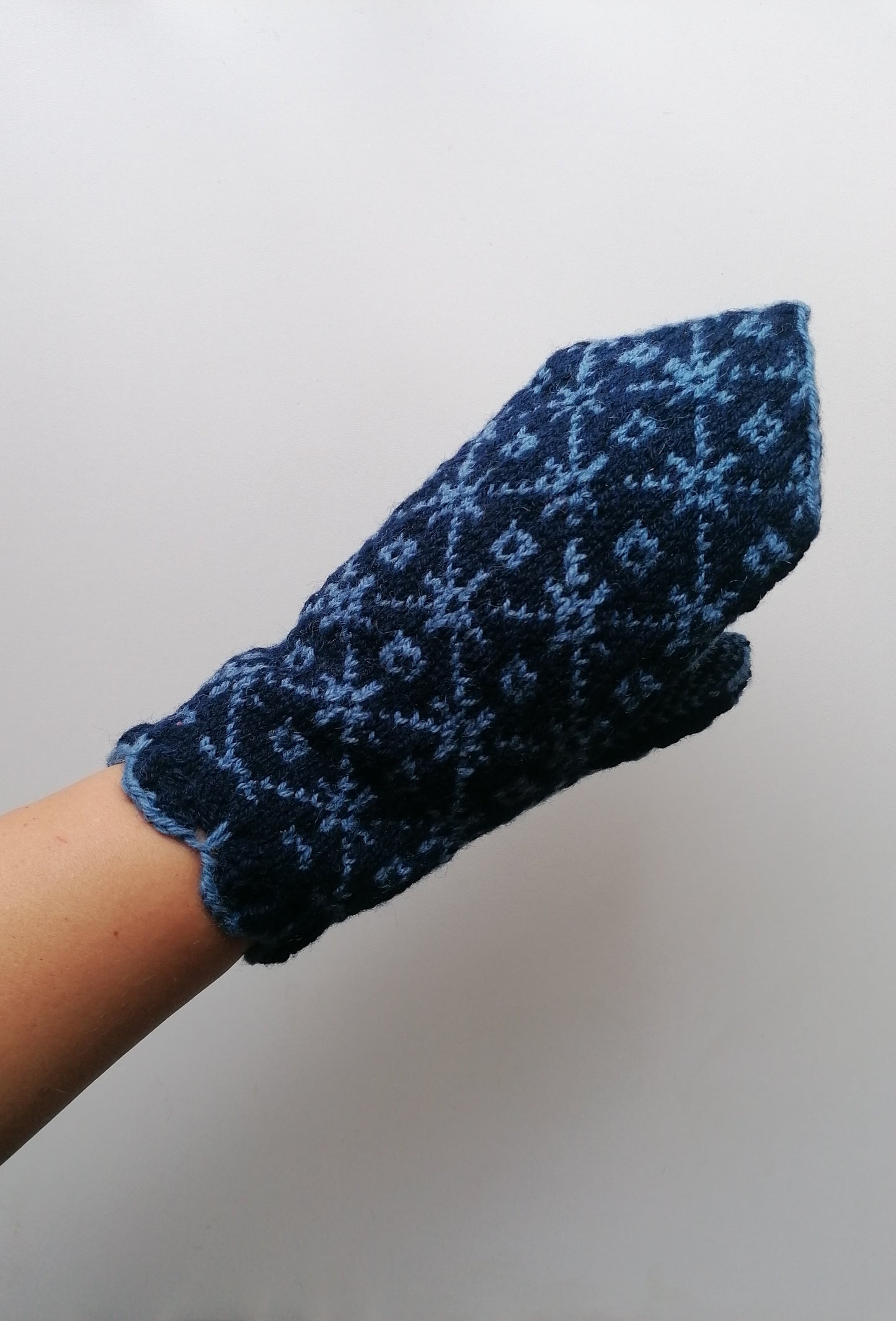 Blue knitted mitten with a pattern held against a plain background