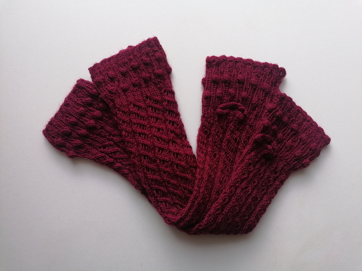 Pair of maroon knitted fingerless gloves on a white background