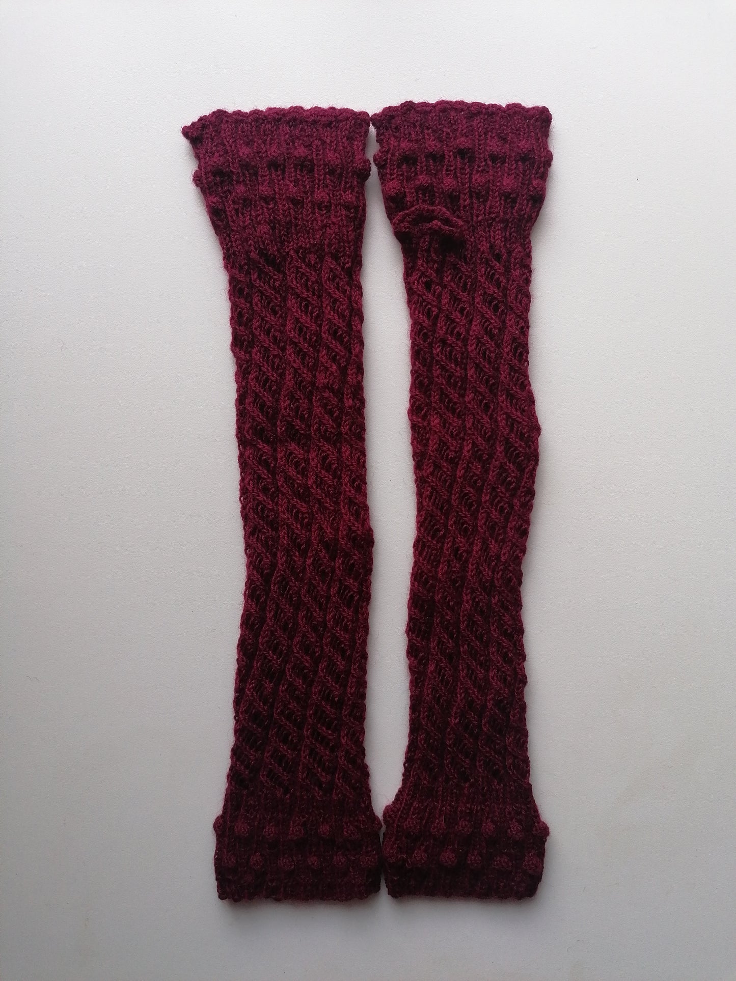 A pair of red-brown knitted fingerless gloves on a white background