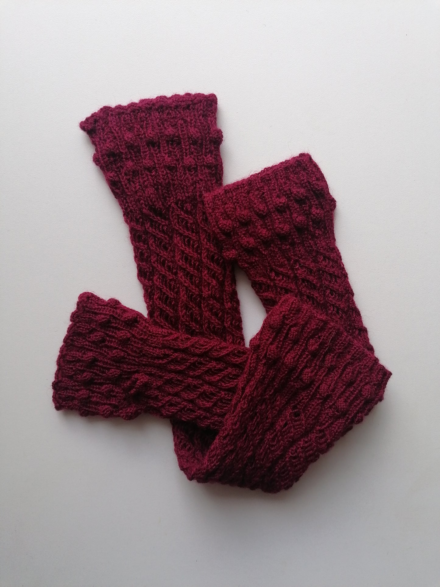 A pair of red-brown knitted fingerless gloves on a white background