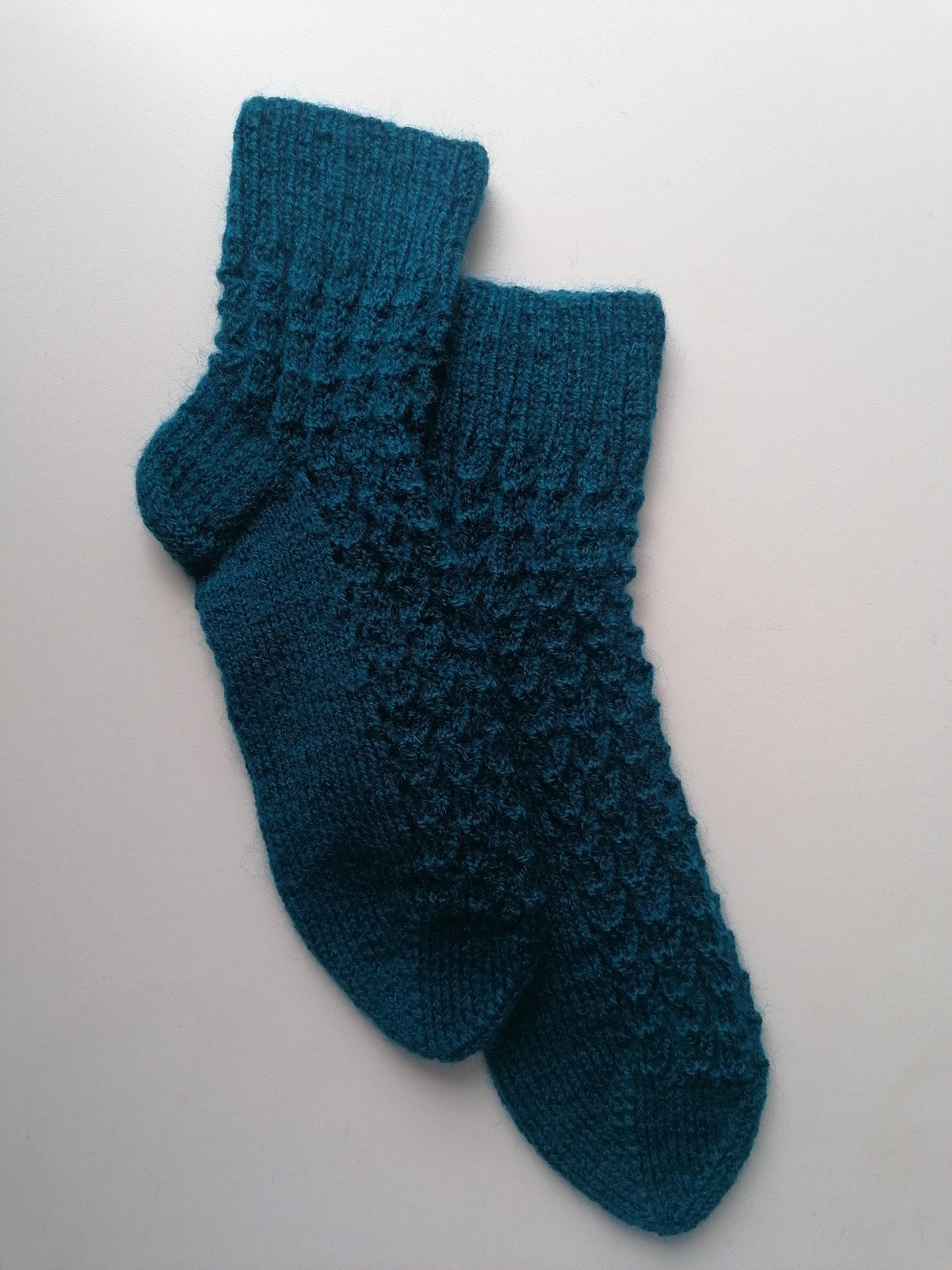 Pair of teal knitted socks on a light gray background