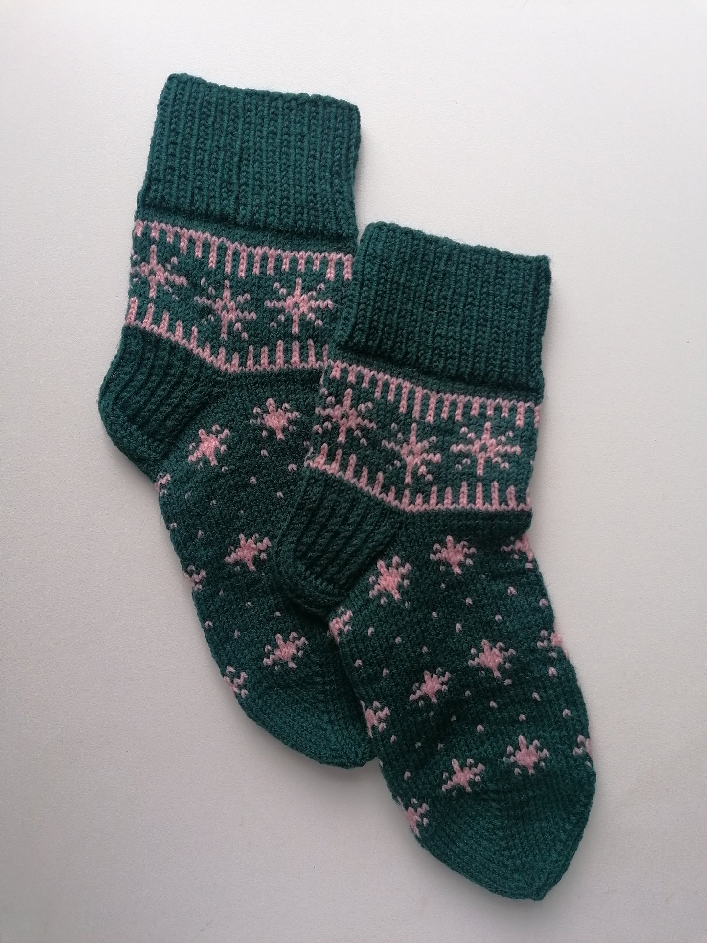Pair of green knitted socks with pink star pattern on a light gray background