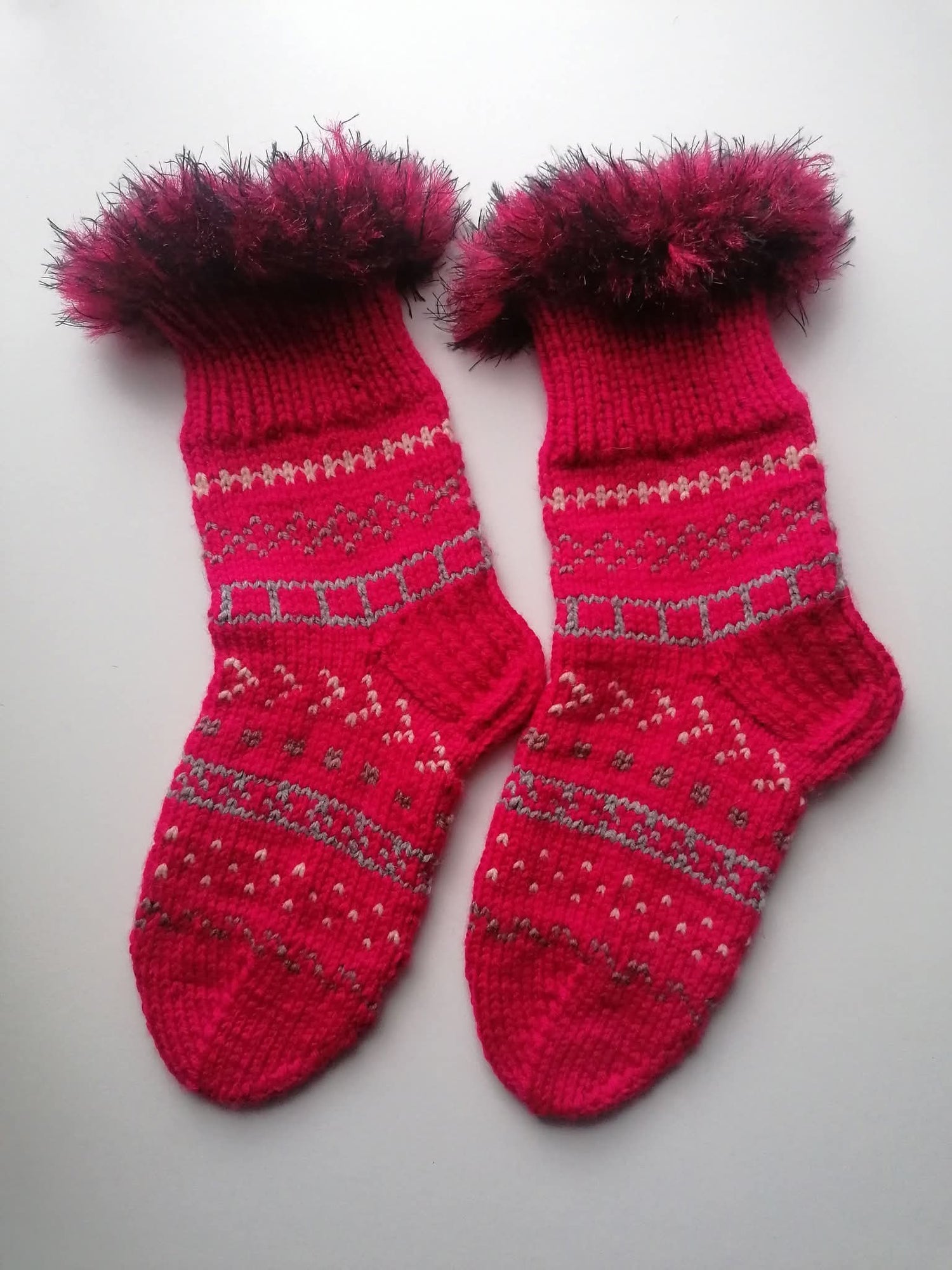Pair of red fluffy knitted socks on a light gray background