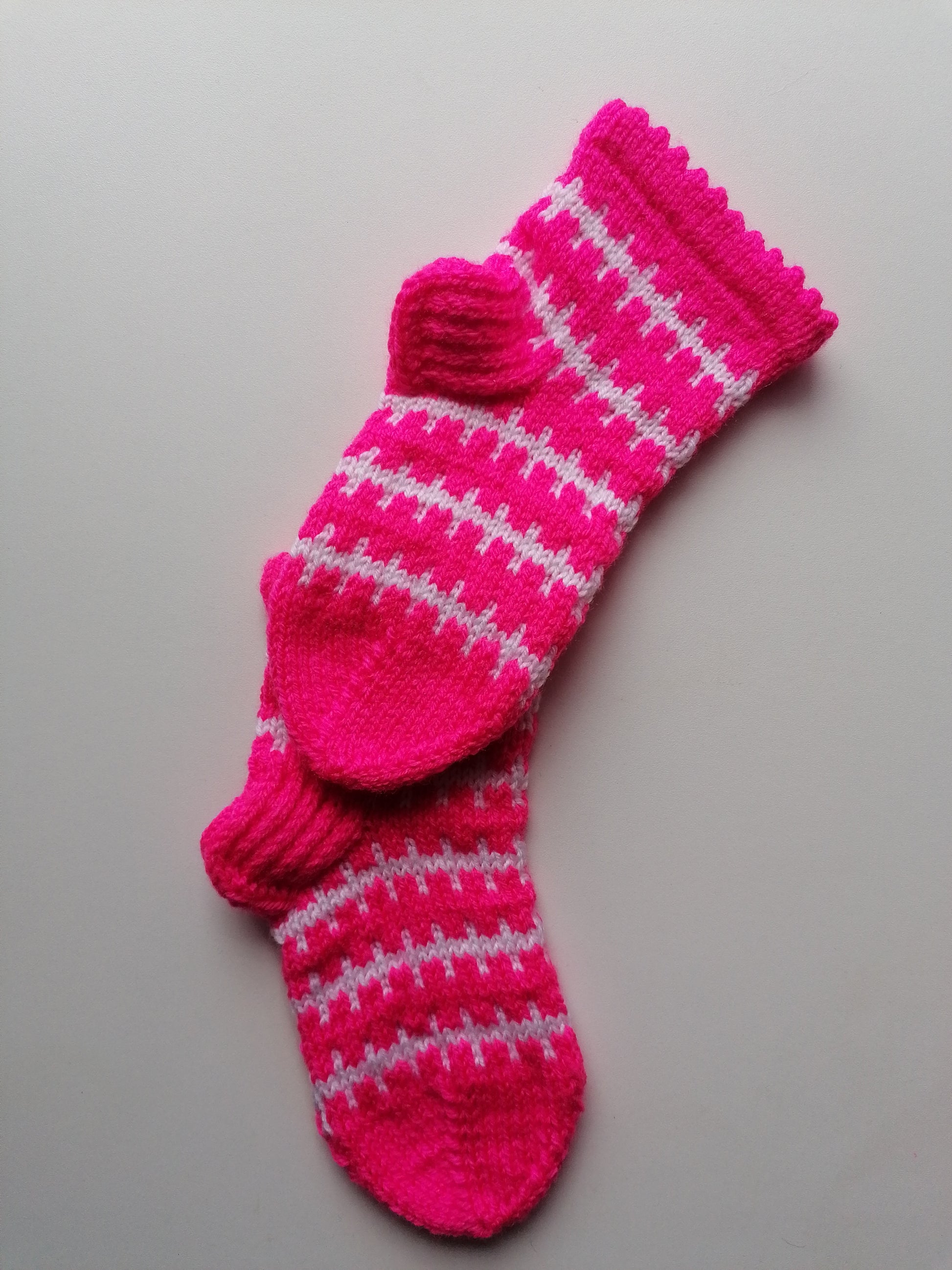 Pair of pink knitted socks with white patterns on a gray background