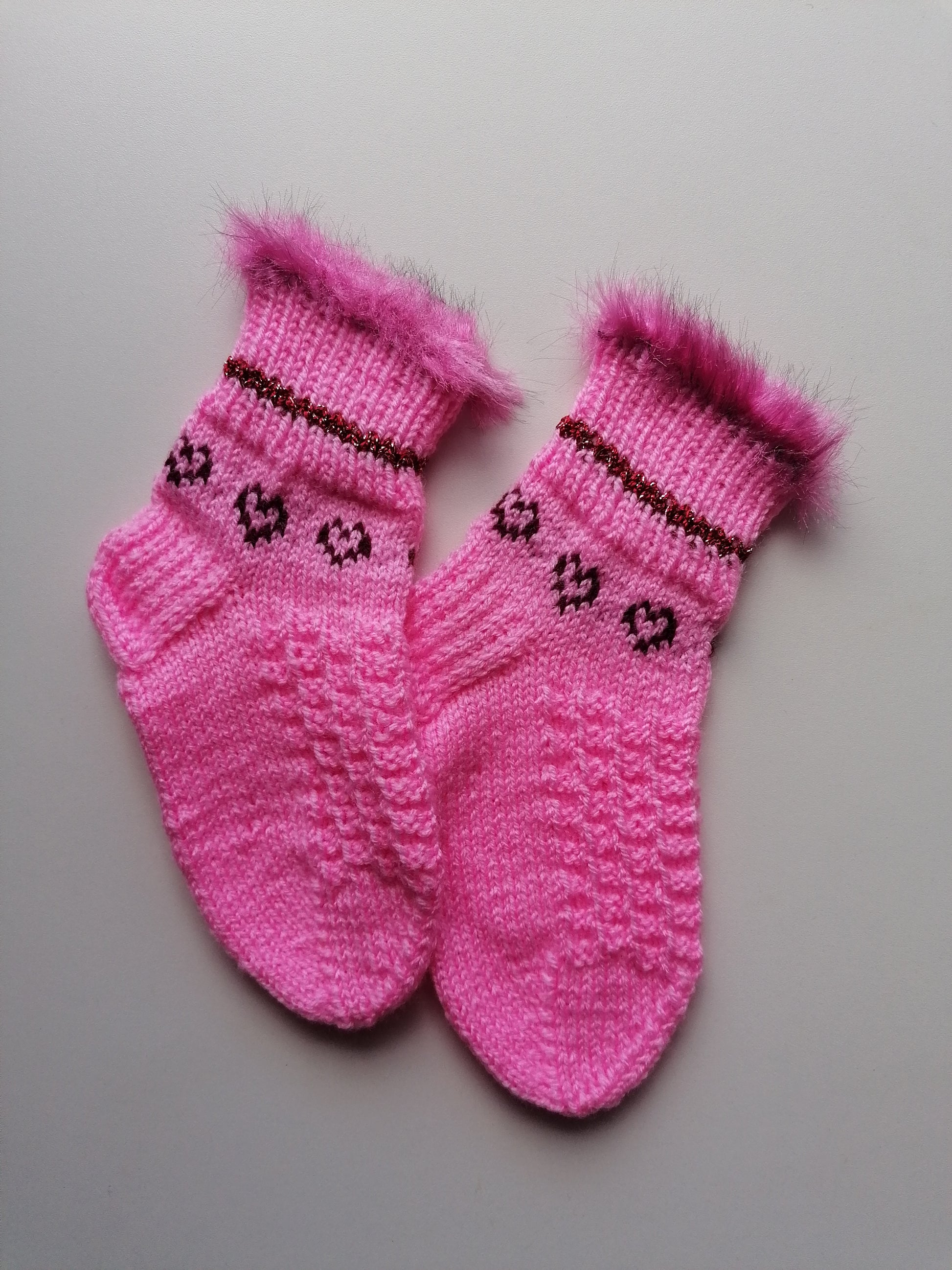 Pair of pink knitted socks with decorative patterns on a light gray background