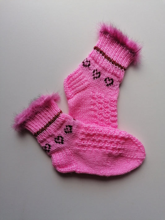 Pair of pink knitted socks with fur trim on a light gray background