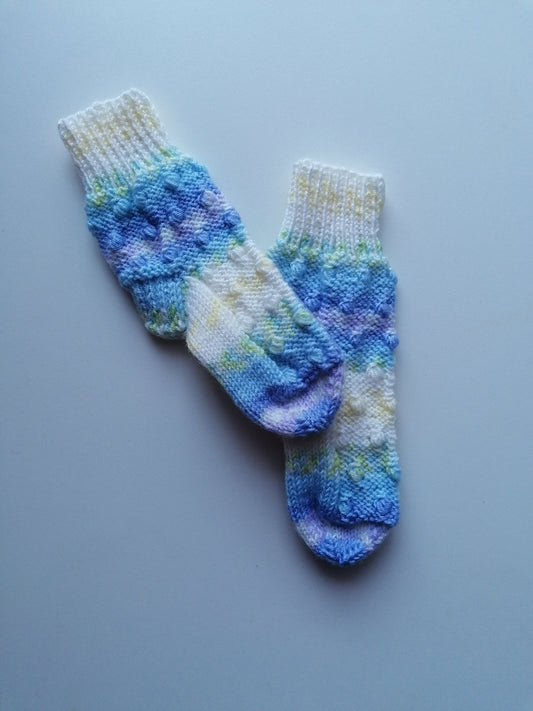 Pair of hand-knitted socks with a blue and white pattern on a light gray background