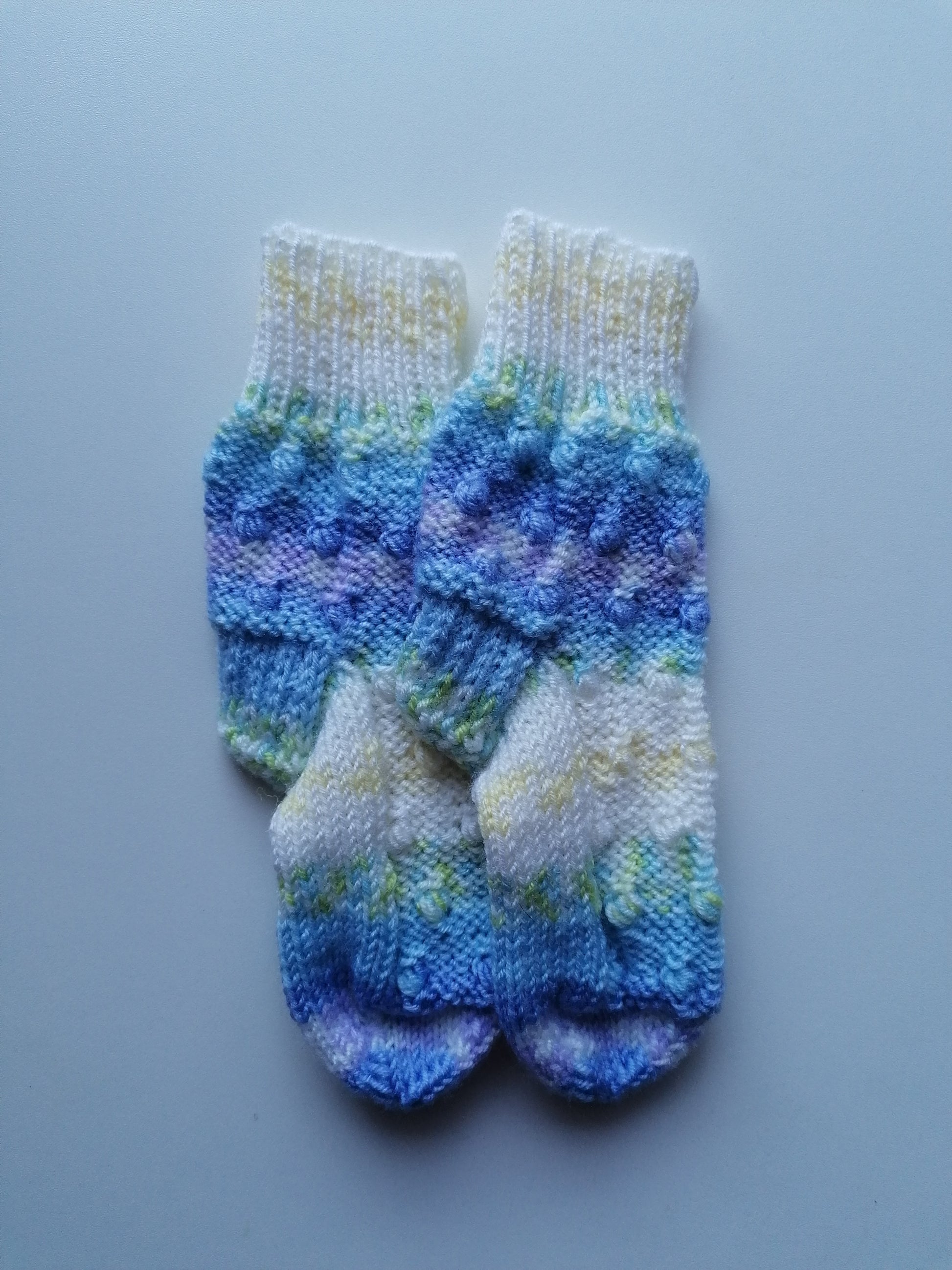 Pair of knitted baby socks with blue and white pattern on a light gray background