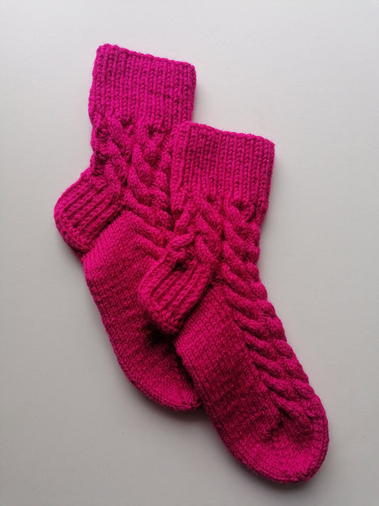 Pair of pink knitted socks wiht braids on a light gray background