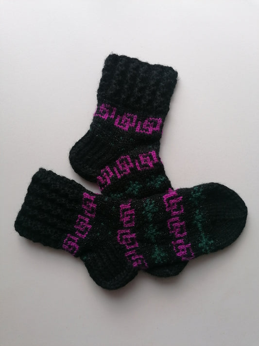 Pair of black and green knitted socks with pink text on a white background