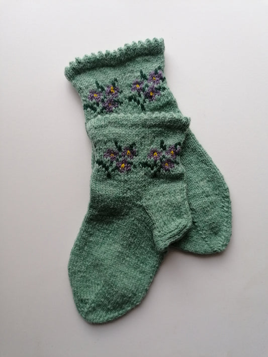 Green knitted sock with floral patterns on a light gray background