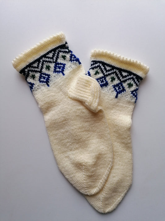 Pair of cream-colored knitted socks with blue and green patterns on a light gray background