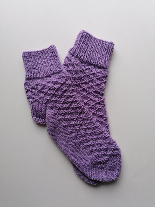 Pair of purple knitted socks on a light gray background