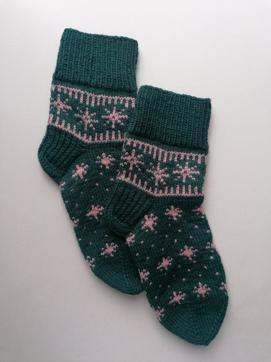 Pair of green knitted socks with pink star pattern on a light gray background